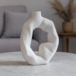 Abstract white vase on a marble table with a gray sofa and plant in the background