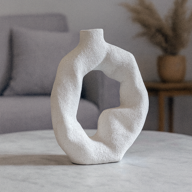 Abstract white vase on a marble table with a gray sofa and plant in the background