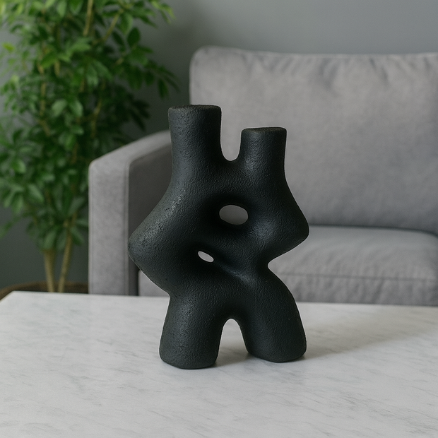Black abstract sculpture on a table with a gray sofa and plant in the background