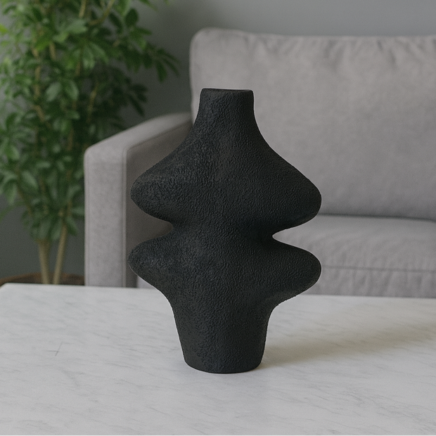 Black textured vase on a table with a gray sofa and plant in the background
