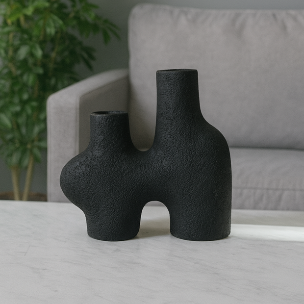 Two black textured vases on a light gray surface with a blurred background