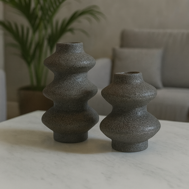 Two textured gray vases on a marble surface with a blurred indoor background